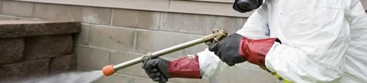 Pest control technician applying exterior insect treatment along a home foundation in Birmingham, AL
