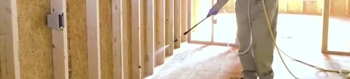 Termite treatment technician applying spray along framing and unfinished walls in Birmingham, AL